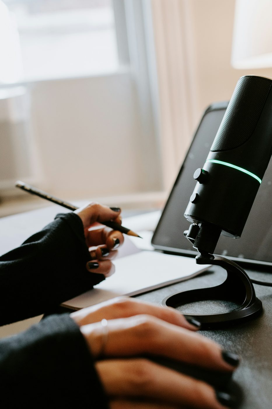 A person writing notes beside a computer and microphone
